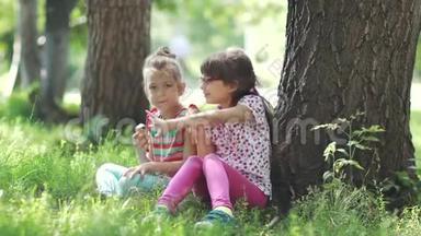 孩子们坐在夏天公园的草地上交谈。 两个小女孩吃<strong>冰淇淋</strong>，享受<strong>夏日</strong>